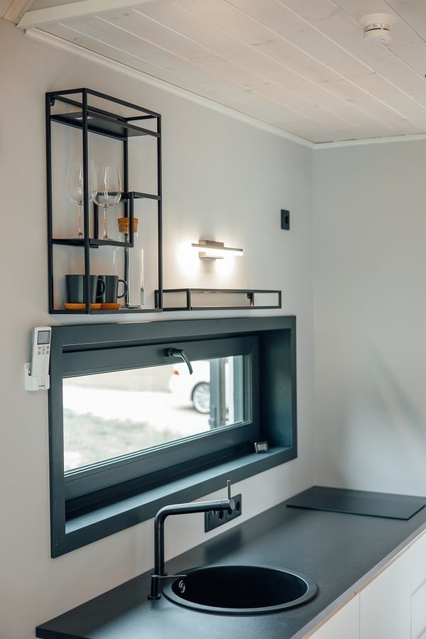 Close-up of kitchen counter with window and wall shelving – Modern black countertop with round sink, open shelves, and a wide horizontal window for natural light.