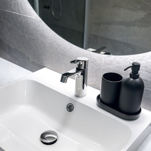 Close-up of modern bathroom sink with chrome faucet and black accessories