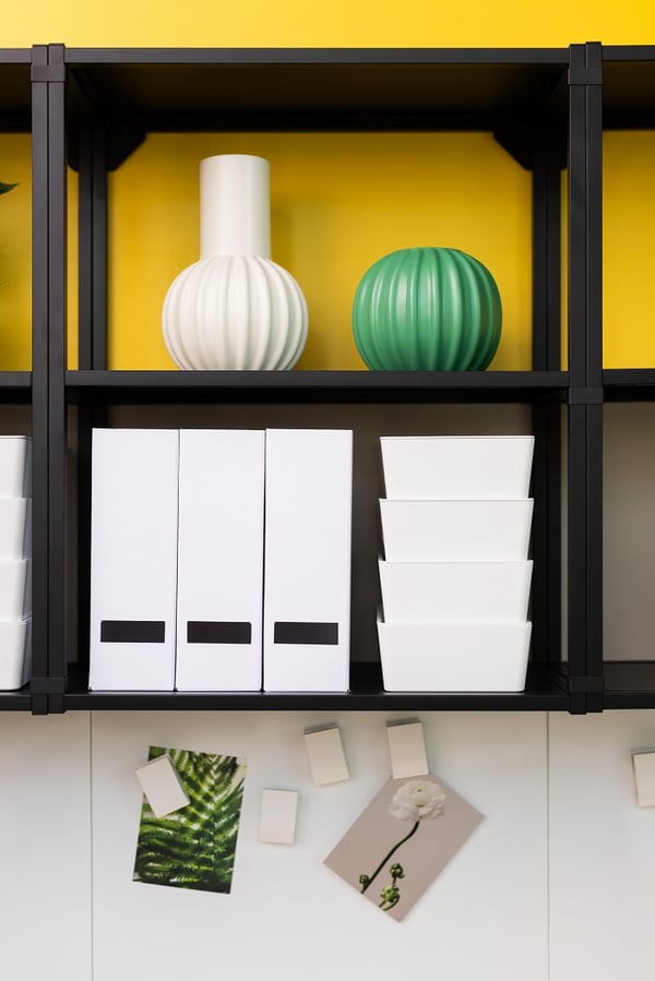 Close-up of office shelving with white storage boxes, decorative vases and yellow background
