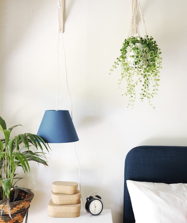 Close up of the corner of a bed and bedside table with small stacked boxes and plants.