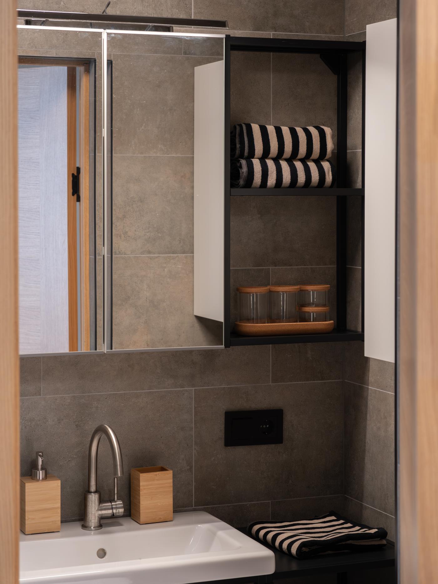 Close-up of the sink area in a modern bathroom, showing a mirror cabinet, striped towels and bamboo accessories.