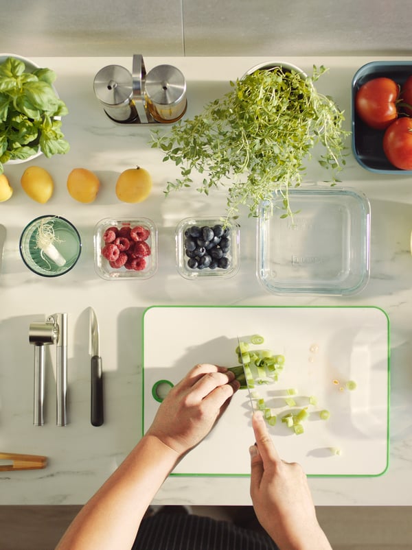 Close-up of two hands  cutting vegetables and of various vegetables, kitchen utensils and food storage boxes.