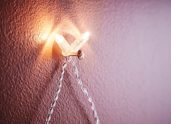 Close-up of two lights on a light chain hanging on a nail on a wall.