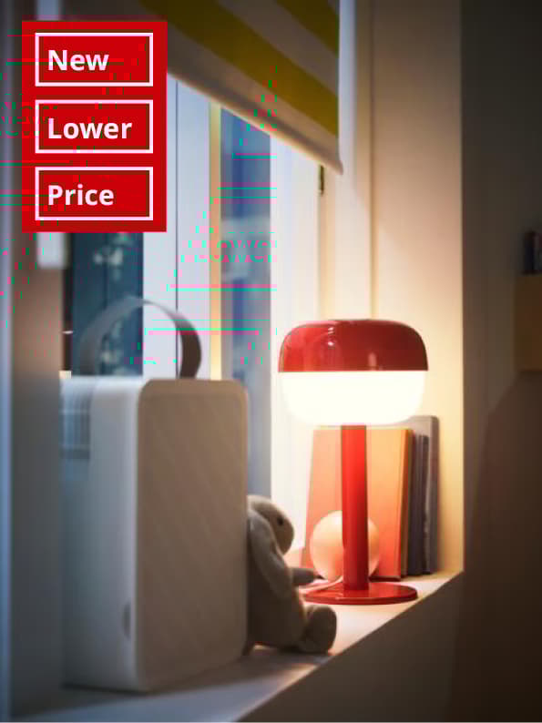 Close-up of window with a block-out roller blind, an UPPÅTVIND air-purifier and a table lamp standing on the window sill.