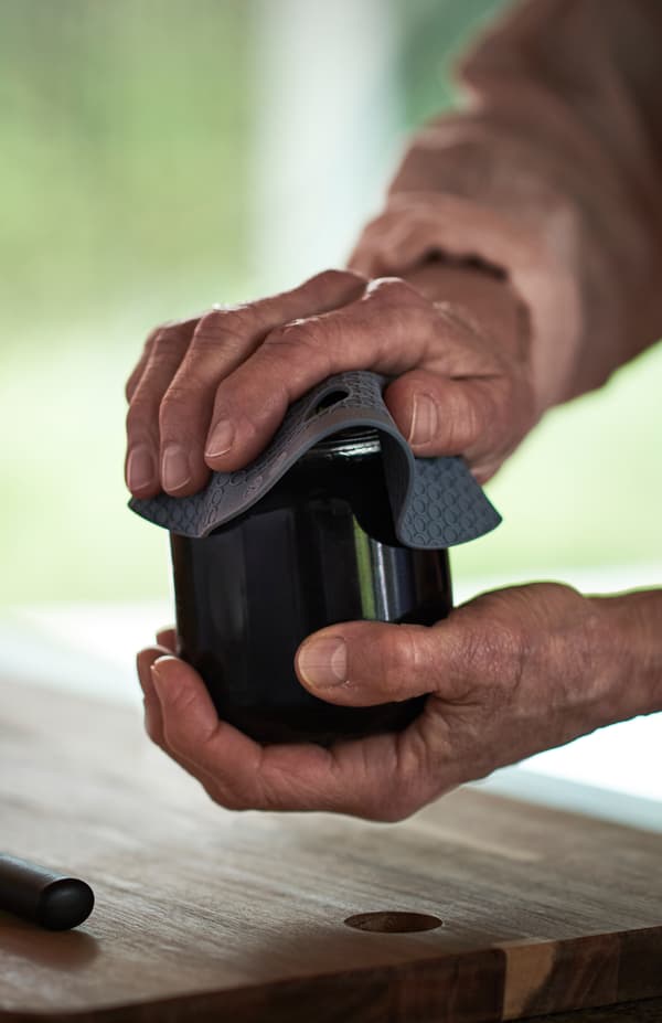 Close-up on a pair of hands using an OMTÄNKSAM jar gripper to open the lid.