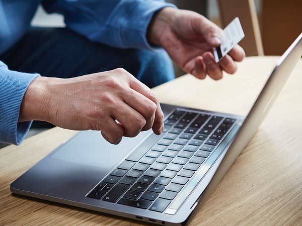 Close-up shot of a person sitting in front of an open laptop with a credit card in their hand.