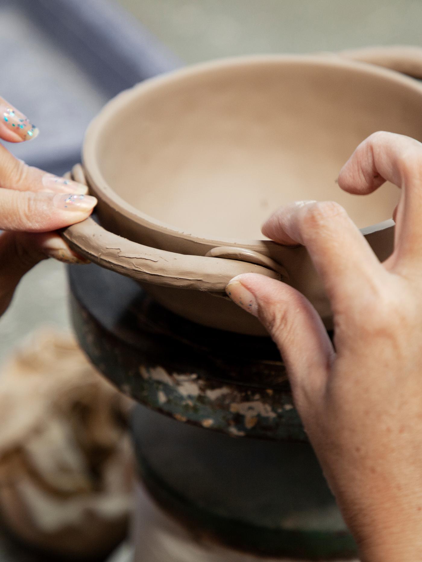 Close-up showing the hands of an artisan attaching a handle to a handmade tall LOKALT ceramic bowl.