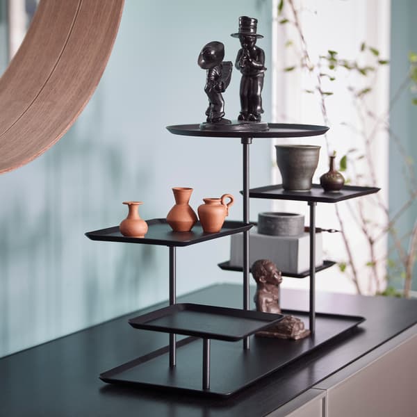 Closeup of black IKEA SAMMANHANG black display stand with square and round pedestal trays holding figurines and items.