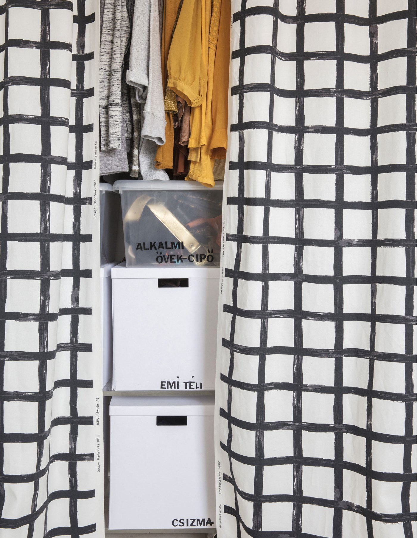 Closeup of white storage boxes in a wardrobe that has black and white curtains instead of doors.