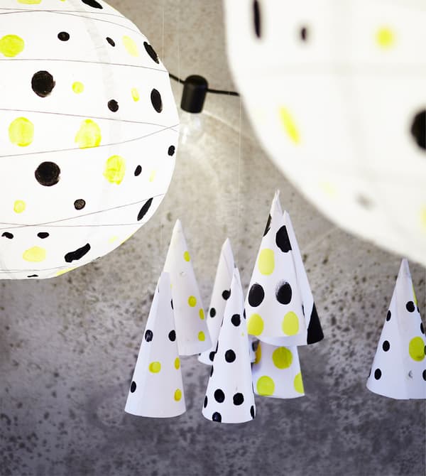 Closeups of circular white paper lanterns decorated with yellow and black dots pasted onto them, including dotted cones.
