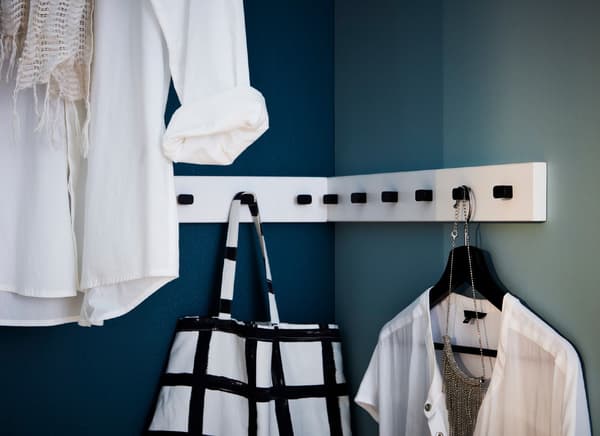 Clothes and bags hanging from knobs in the corner of a room.