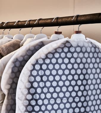 Clothes are stored in clothing bags and hung on a rack in  an attic.