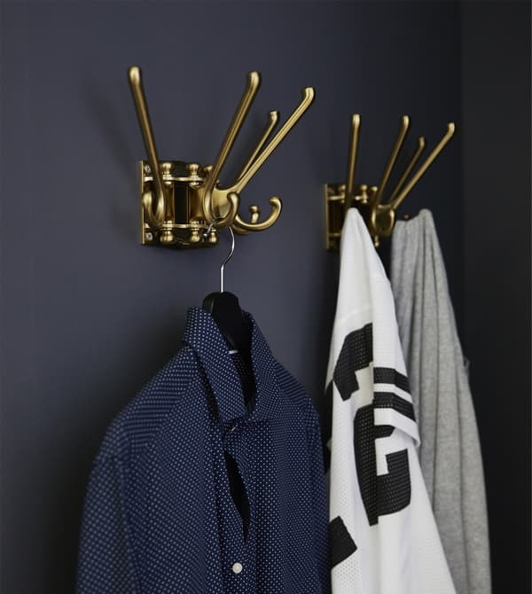 Clothes hang from two KÄMPIG 4-armed swivel hooks mounted on a dark grey wall.