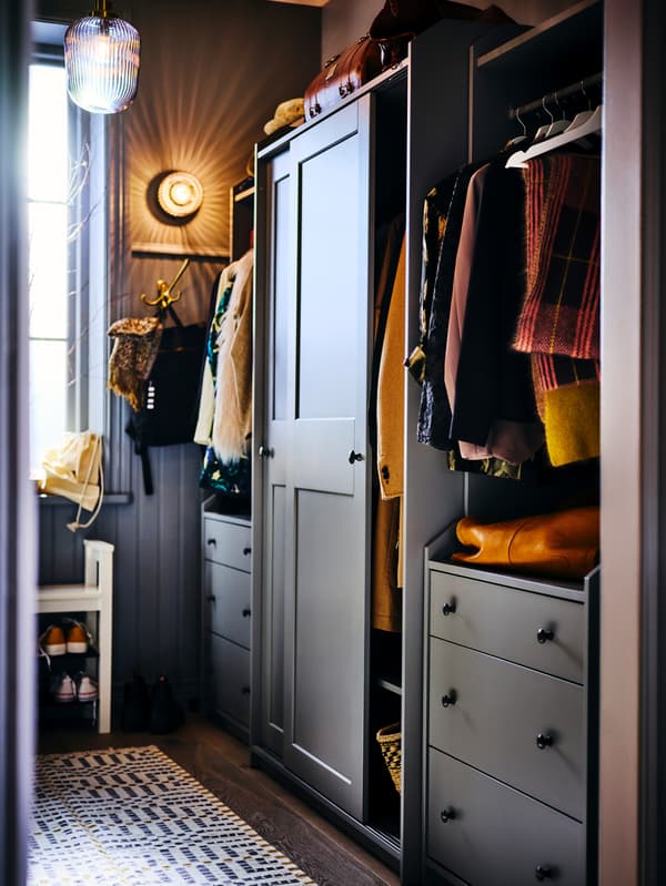 Clothes hang in a grey HAUGA wardrobe combination that has one door partly open, other items are stored on the top surface.