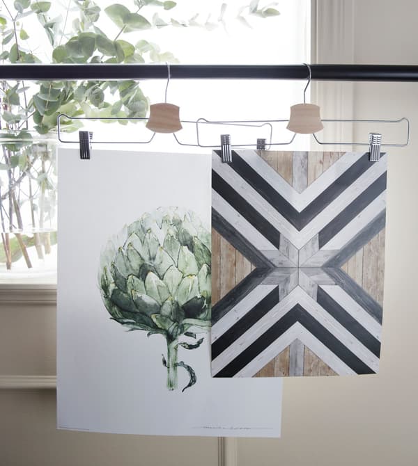Clothes hangers with artwork pegged to them, in front of a window.