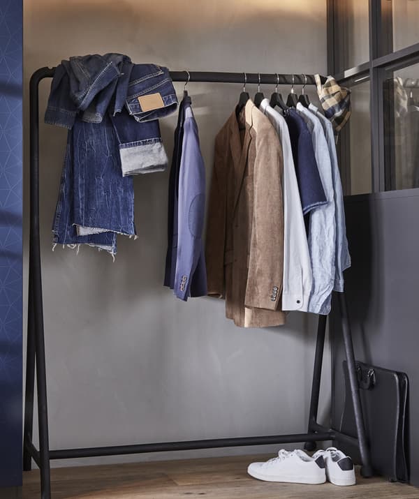 Clothes hanging on a black open clothes rail against a pale grey wall.