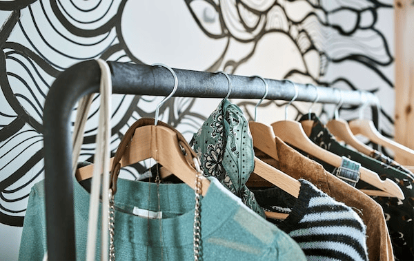 Clothes hanging on wooden coat hangers on a clothes rail placed in front of wavy black and white wallpaper.