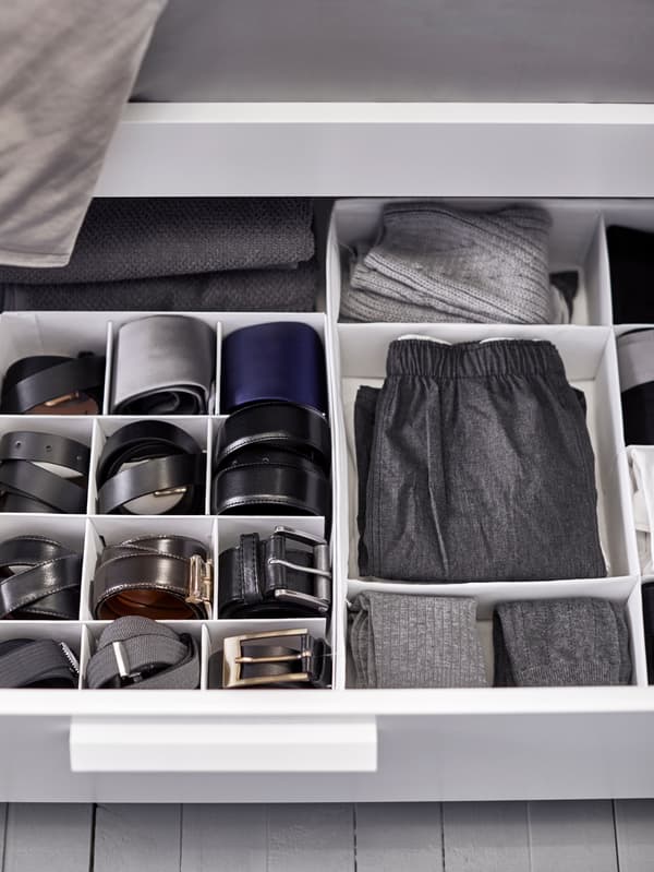 Clothing and belts arranged neatly in interior organisers inside a drawer under a bed.
