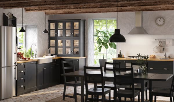 Cocina de estilo escandinavo tradicional de IKEA con mesa negra, sillas negras y muebles de cocina negros, encimera en madera natural y lámnparas de metal.