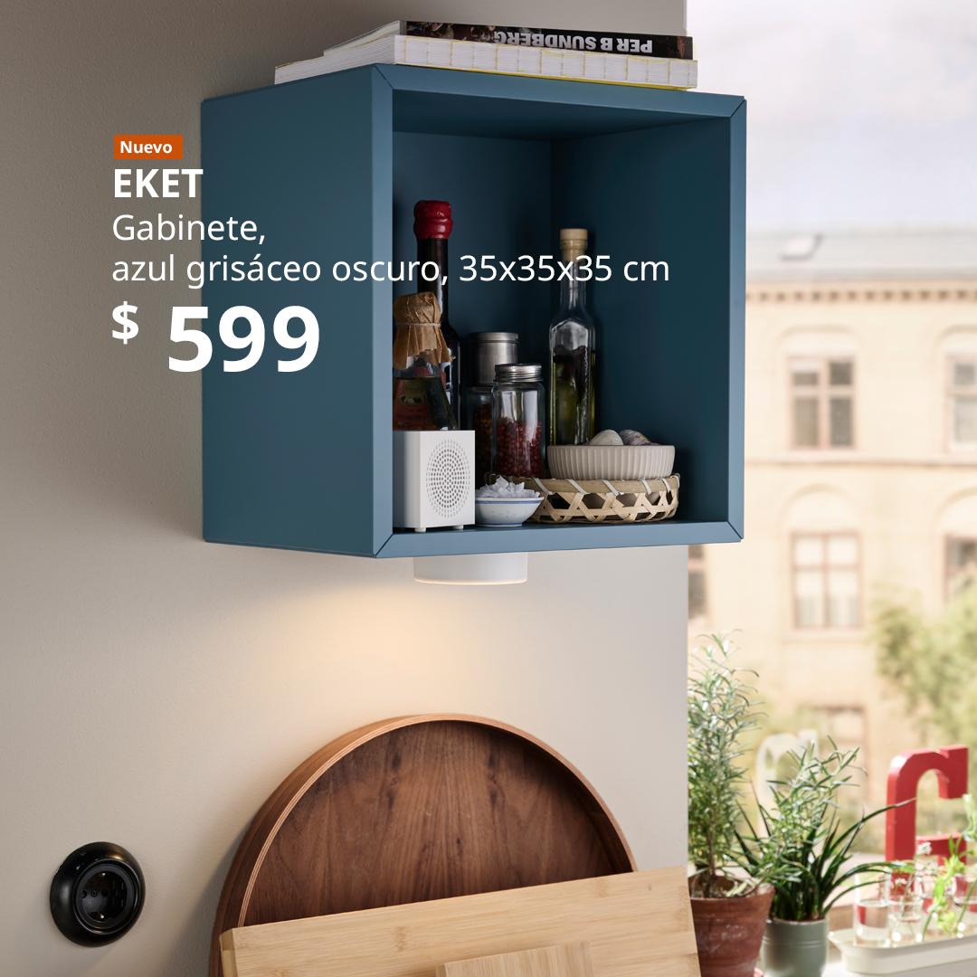Cocina moderna con gabinete de pared EKET azul, estante abierto con botellas, especias, canasta con tazones y dispositivo electrónico, tablas de cortar de madera debajo y lámpara integrada; diseño funcional y decorativo para almacenamiento