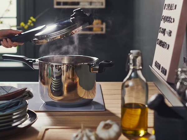 Cocotte cuisant sur une plaque, une main tient en l'air le couvercle et la vapeur se dégage de la cocotte.