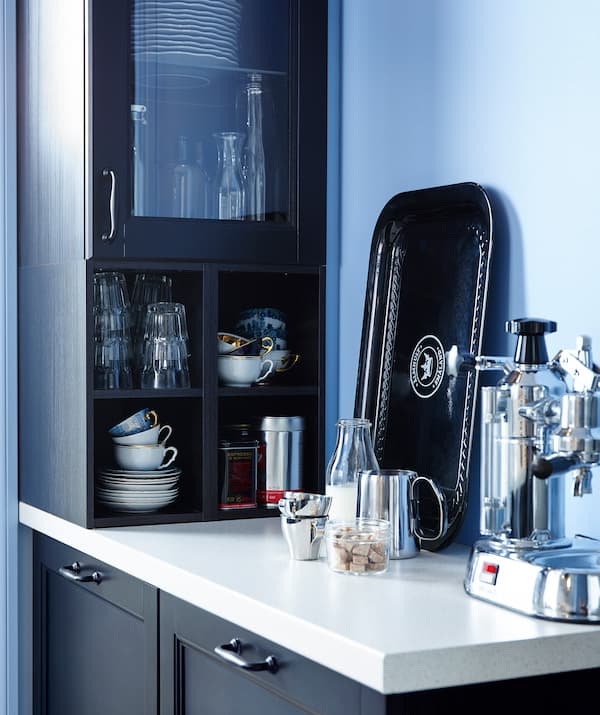 Coffee machine on a narrow IKEA worktop. Wall cupboard holding cups, coffee and glassware.