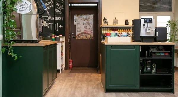 Coffee station with green cabinets, espresso machine, and colorful mugs in a cozy café interior.