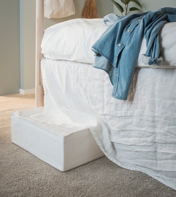 Coffre de rangement placé sous le lit, dissimulé par le juponnage