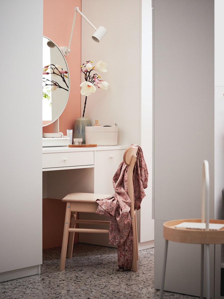 Coin beauté avec une coiffeuse SYVDE blanche dans un coin peint en rose saumon sur lequel est fixé un miroir rond et une lampe . Sur la coiffeuse se trouve une orchidée artificielle et une boîte à bijoux