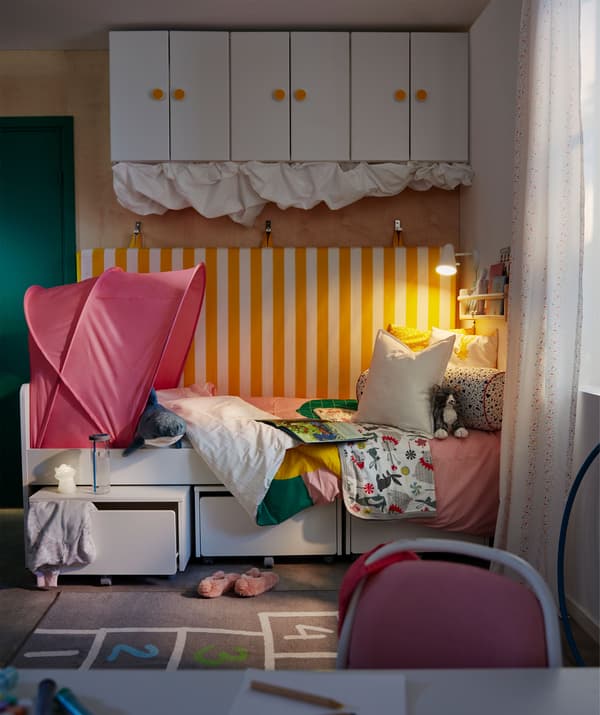 Coin dodo dans une chambre d’enfant. Un matelas est accroché au mur derrière le lit, on trouve aussi du rangement sous le lit et au mur.