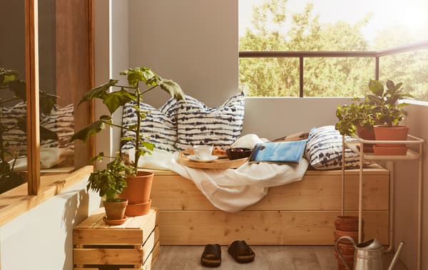Coin d’un balcon avec un caisson en bois sur lequel se trouvent des coussins, du linge de lit et un petit déjeuner servi sur un plateau.