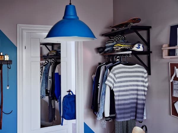 Coin d’une chambre avec miroir sur la porte et vêtements sur des étagères et sur une tringle 