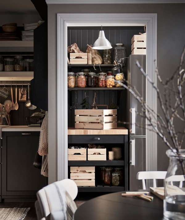 Coin garde-manger, desserte de cuisine avec des caisses en bois dans un coin, sous des étagères portant des bocaux en verre.