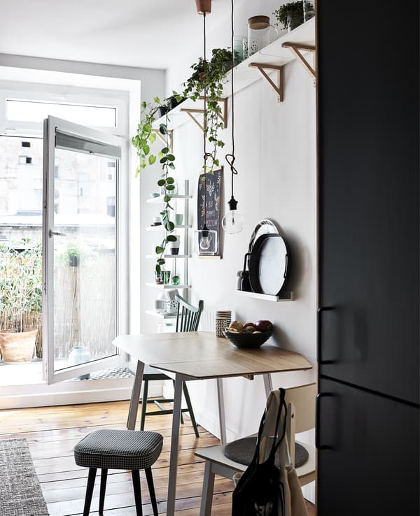 Coin repas blanc avec plantes sur une étagère en hauteur et porte ouverte.