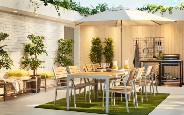 Coin repas extérieur moderne avec deux tables SJÄLLAND 8 chaises en gris clair/brun clair dans un jardin clôturé.