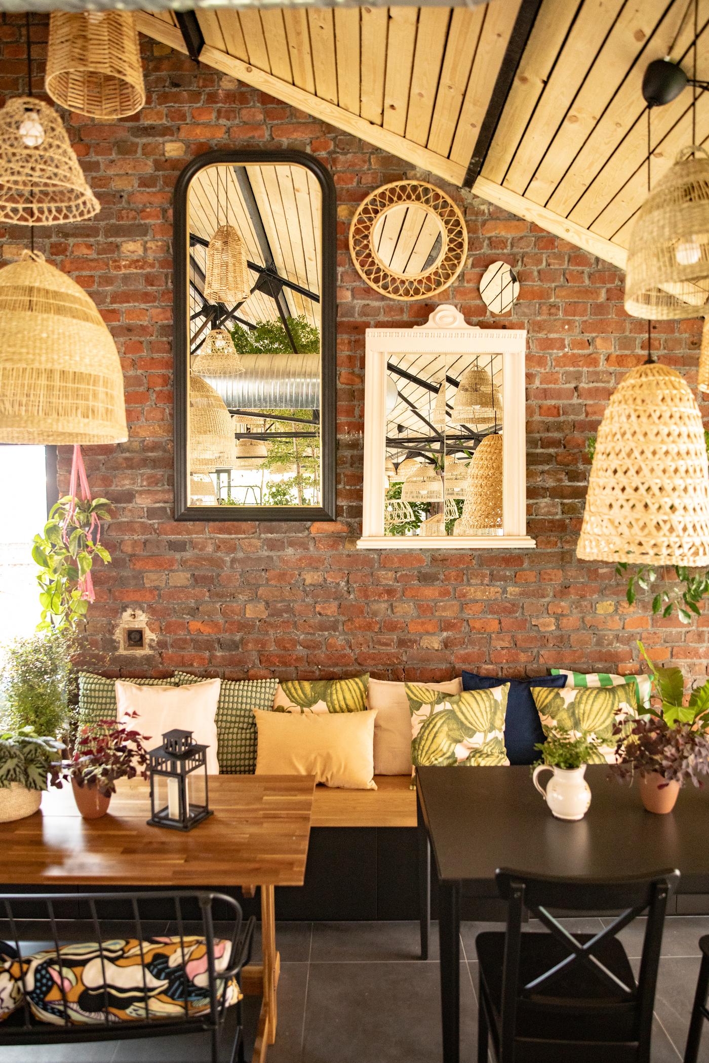 Coin restaurant mansardé avec des miroirs muraux, un banc avec plusieurs coussins et des tables en bois pour 4 et 2 personnes.