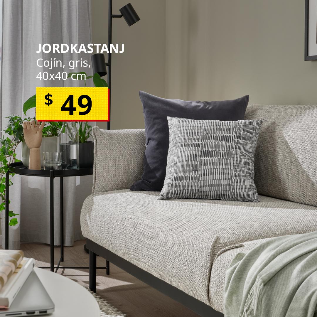 Cojín JORDKASTANJ gris colocado sobre un sofá color beige, acompañado de otros cojines en tonos grises.