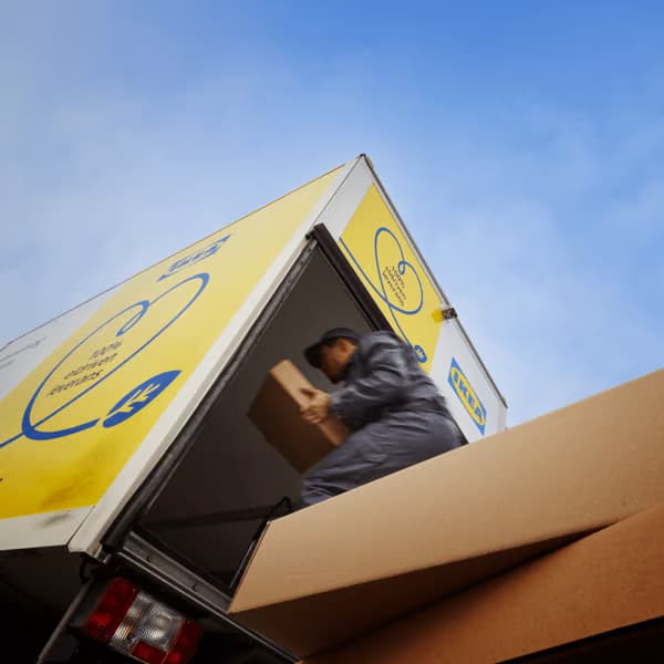 Colaborador cargando una caja de cartón en un camión de reparto IKEA bajo un cielo azul.