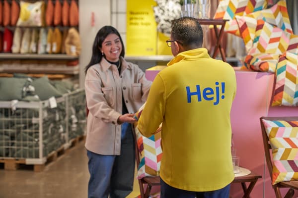 Colaboradora con chaqueta amarilla de IKEA sosteniendo un cojín, frente a el un cliente con una sonrisa en la cara.