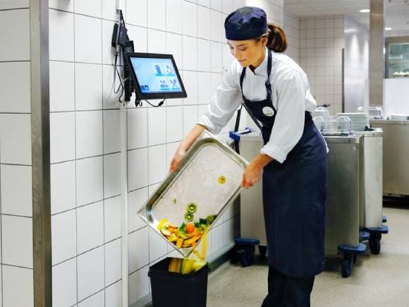 Colaboradora de la cocina de nuestro restaurant botando los residuos de alimento al contenedor después de haberlos ingresado al sistema.