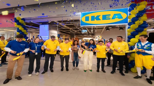 Colaboradores de tienda IKEA cortando la cinta frente a la entrada de la nueva tienda en Cali con un logo IKEA arriba iluminado, globos amarillos y azules y confetti de los mismos colores como decoración.
