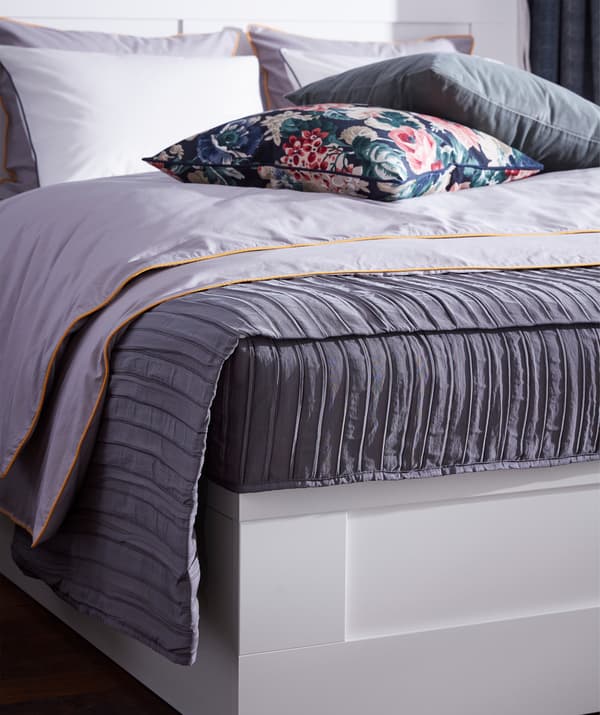 Colcha de tecido acolchado lila IKEA VEKETÅG con deseño plisado sobre unha cama.