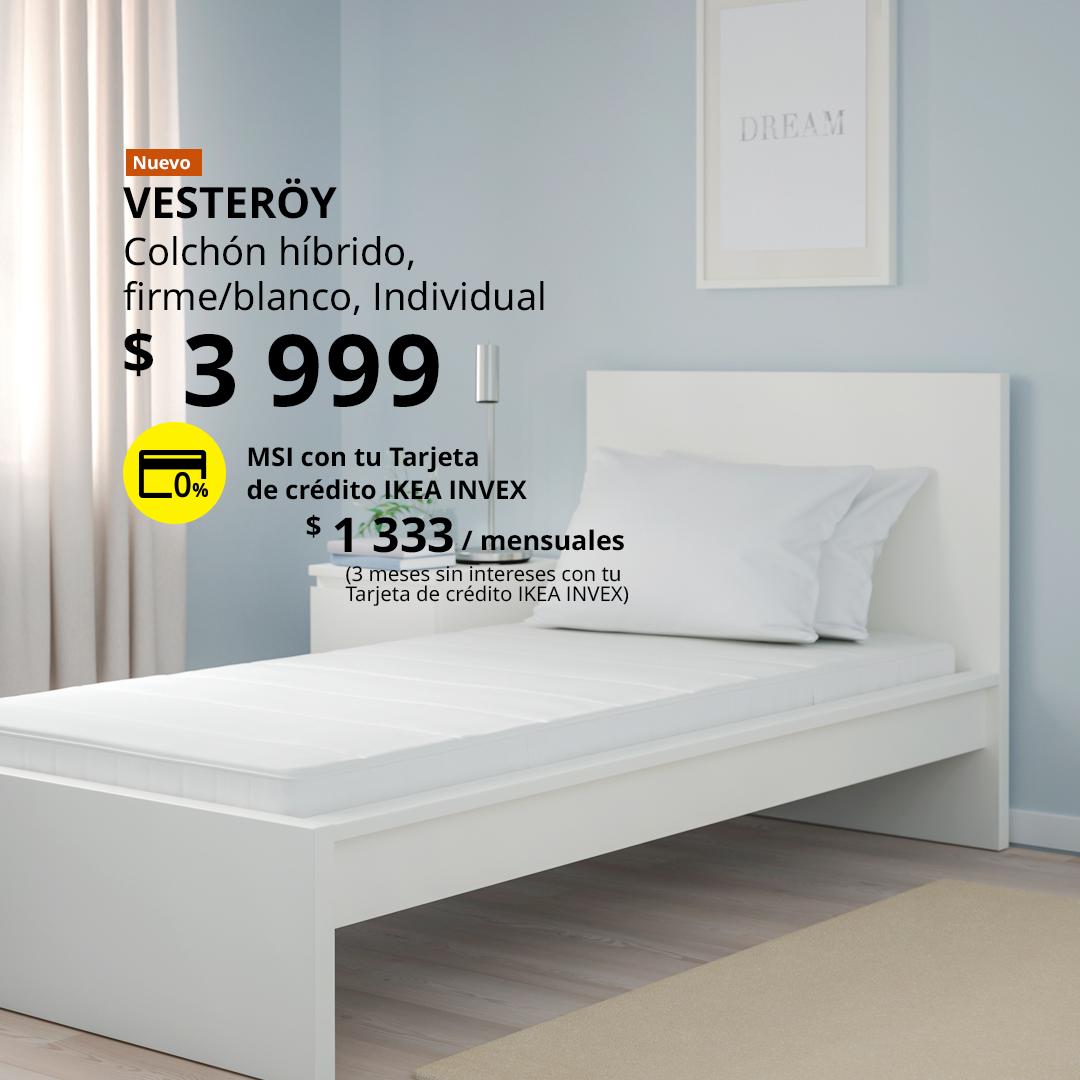 Colchón híbrido VESTERÖY firme en color blanco sobre una cama blanca en un dormitorio de tonos azul claro.