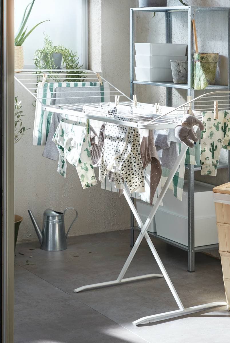 Colgante de ropa MULIG blanco, junto a una cesta de ropa hecha de bambú en una zona de lavado de ropa.