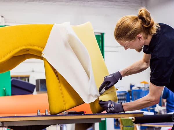 Collaborateur IKEA portant un t-shirt noir et des gants de travail. Il rehousse un fauteuil à l’aide d’un textile jaune vif. 