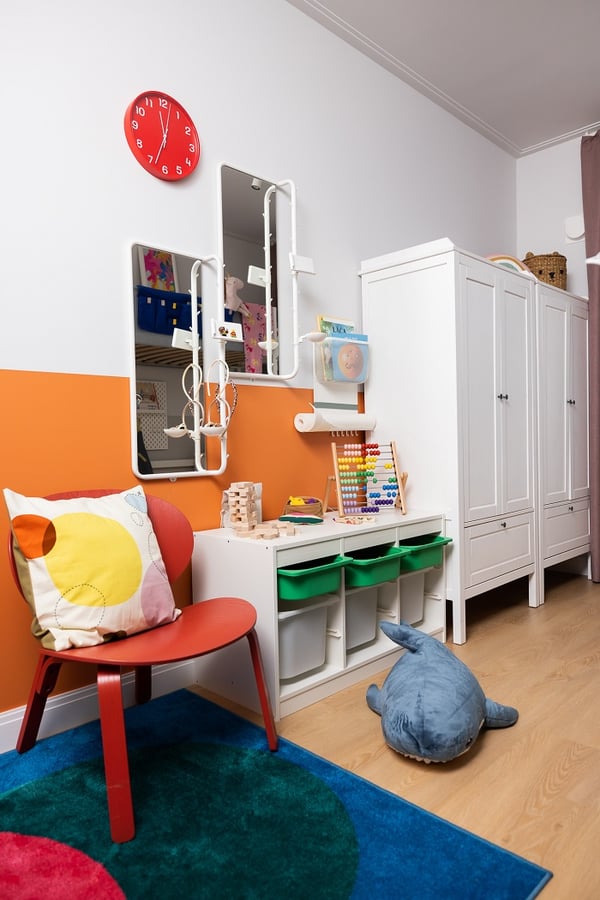 Colorful children’s playroom with orange wall, red chair, toy storage, and abacus.