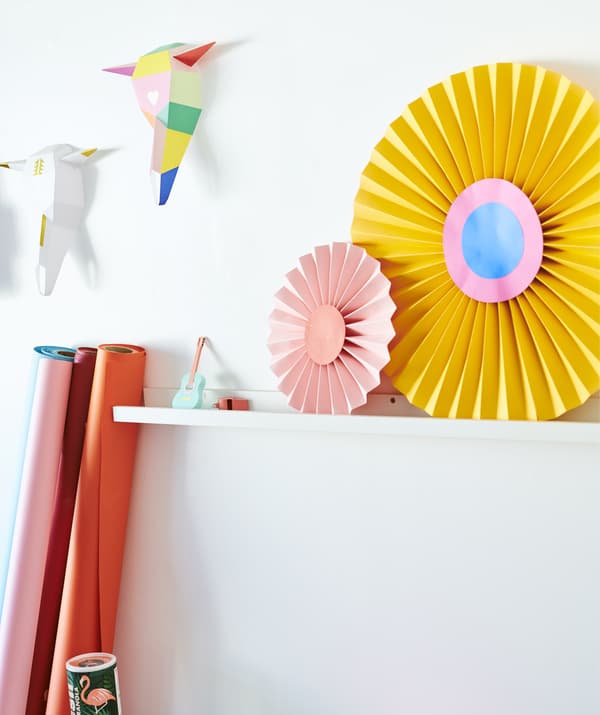 Colorful paper shapes displayed on a white picture ledge on a white wall.