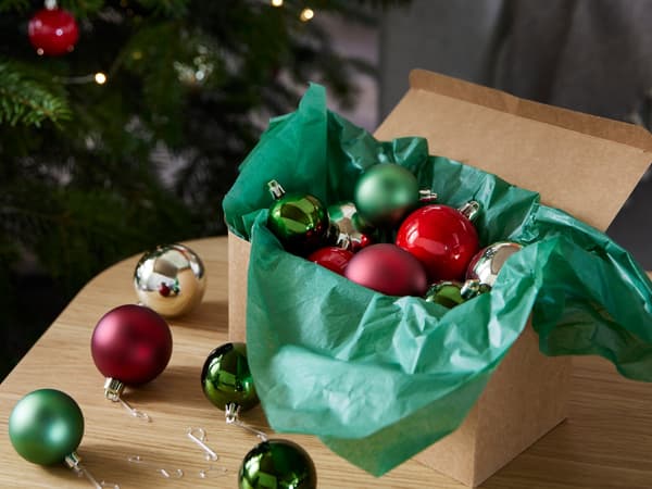 Coloured christmas baubles in a box in front of a christmas tree