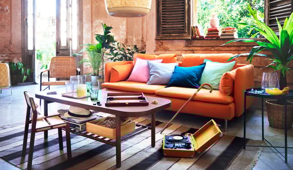 Coloured cushions placed on an orange SÖDERHAMN sofa in a living room. A coffee table holds drinks and a board game.