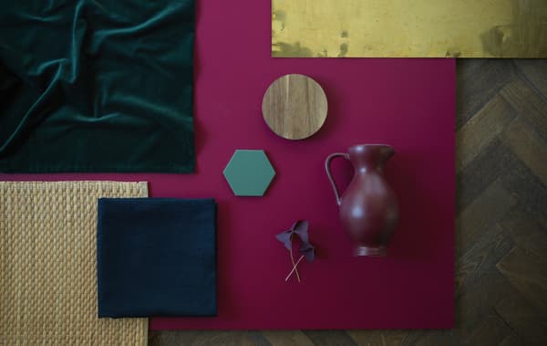 Colourful floor-mats, tablemats, textiles and a vase laid out on a wooden floor.